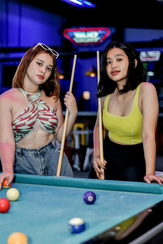 two beautiful young women holding up stick of pool