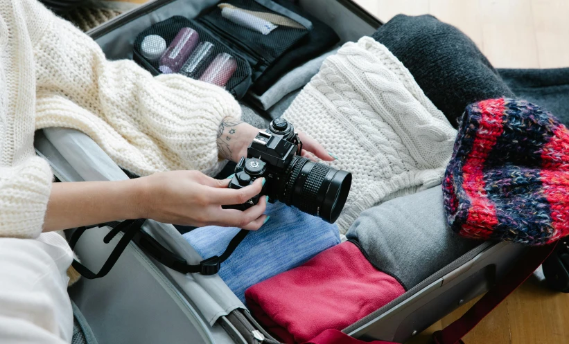 a woman holding a camera and sitting in a suitcase