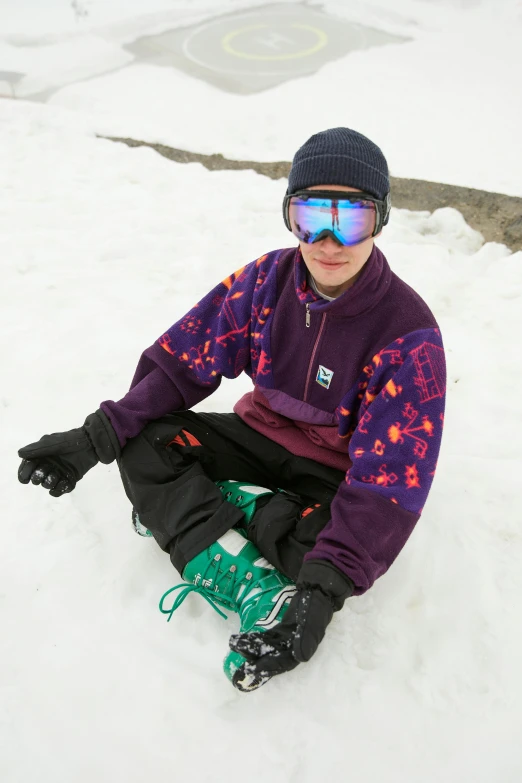 a young man sitting in the snow wearing ski goggles