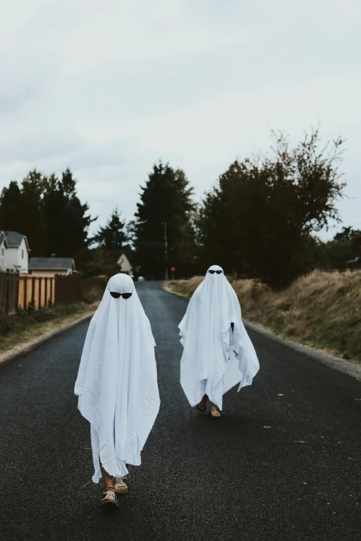 two people in white ghost costumes walk down the middle of a street