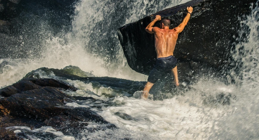 a shirtless male is reaching up to get some air in a wave