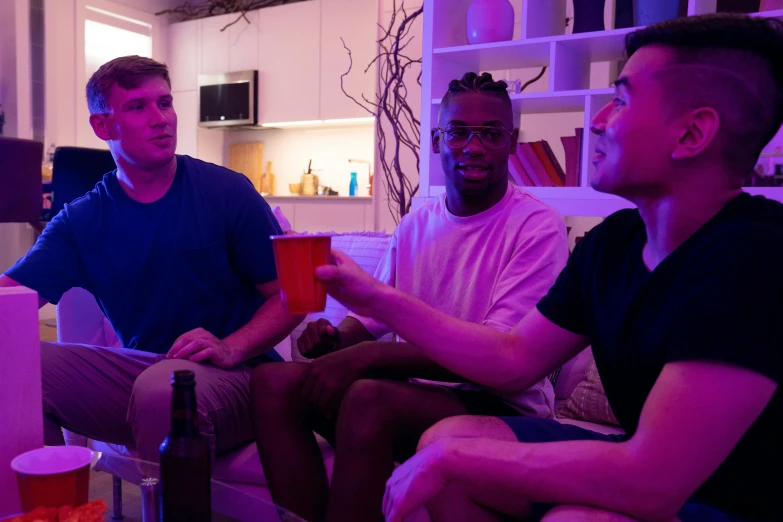 three men sitting in front of a television and a couch talking