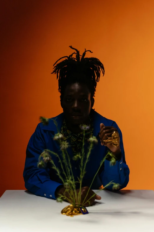 a man sits at a table holding a flower vase with a plant in it