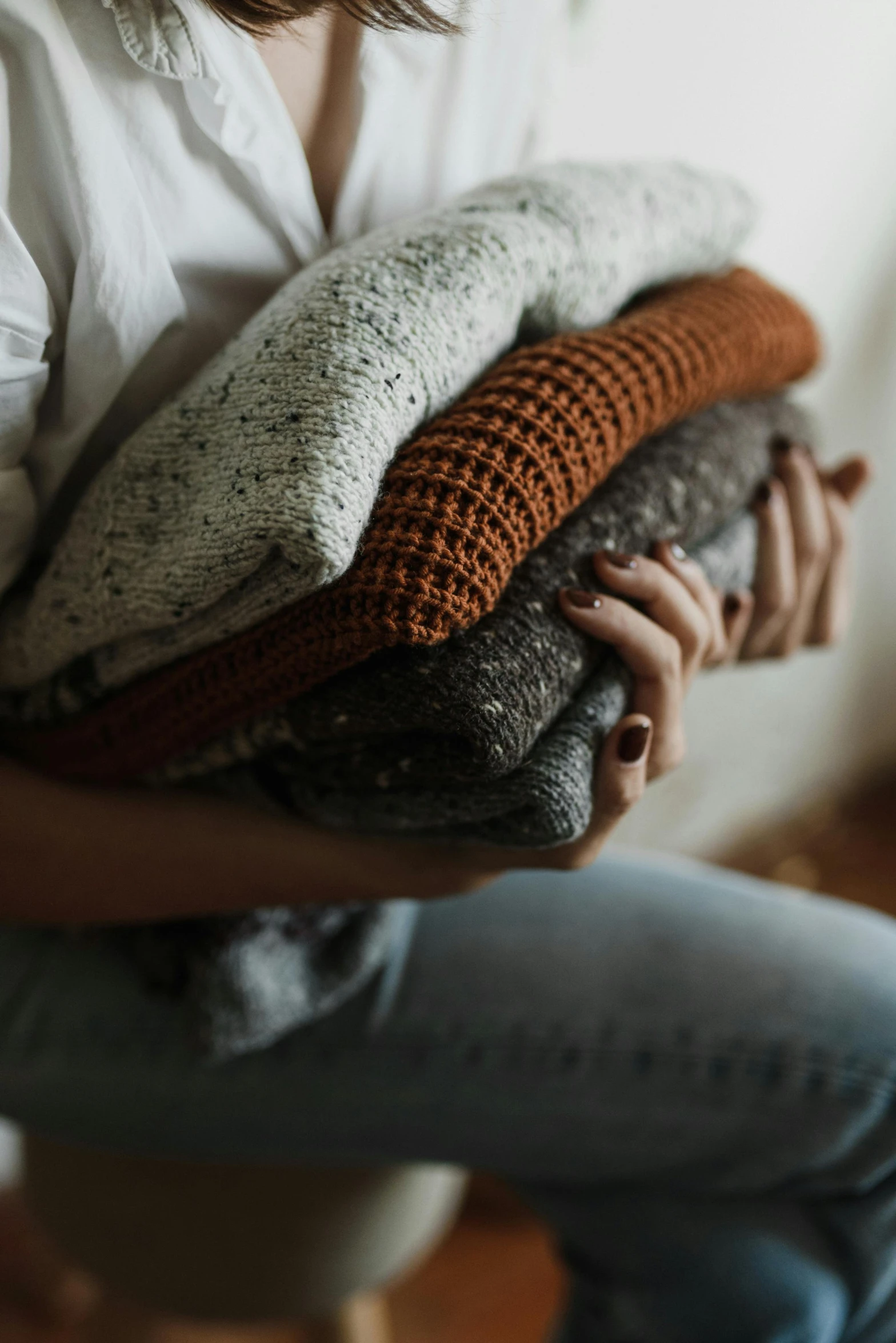 a woman is sitting down holding some sweaters