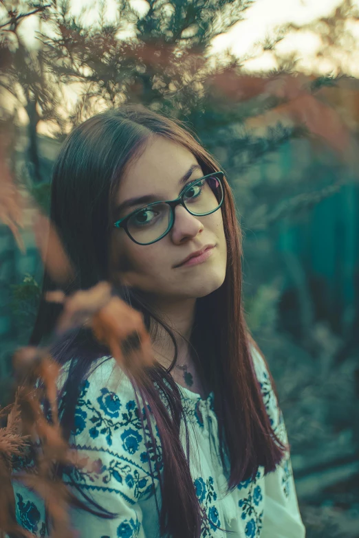 a beautiful young lady with glasses standing near plants