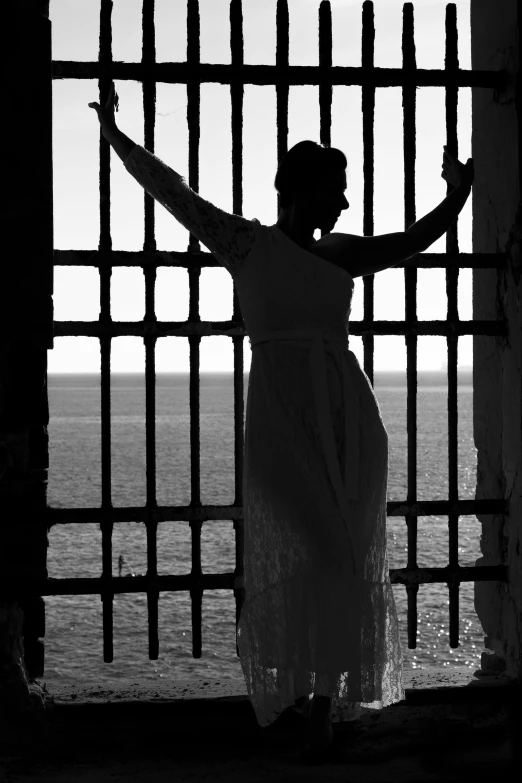 woman in white dress stands outside a barred iron gate