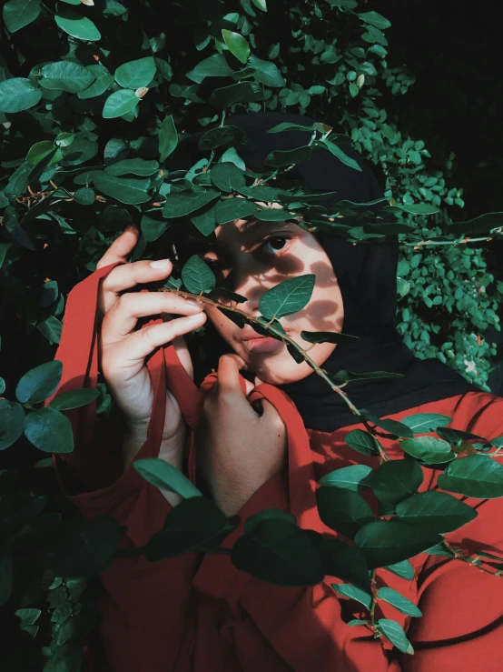 a young woman is hiding under leaves in a garden