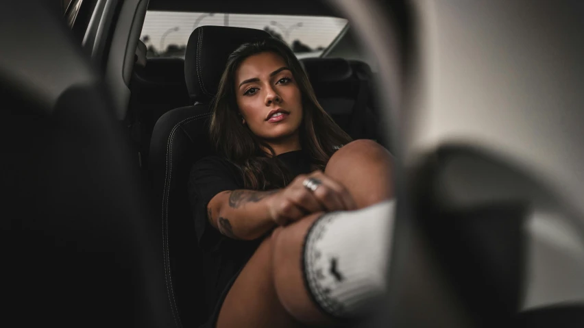 a girl in a car sitting and holding her arm on the steering wheel