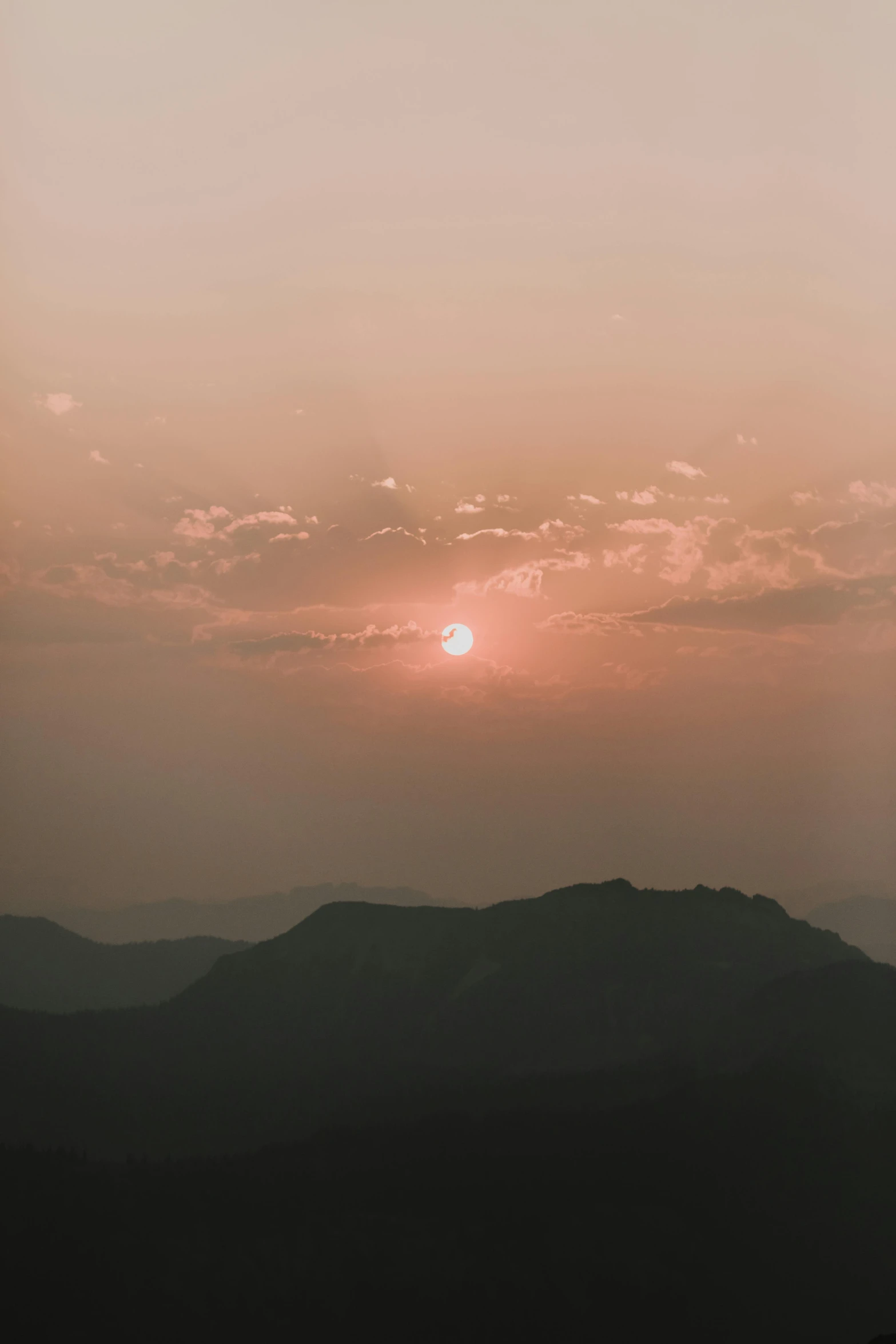 the sun setting over a mountain range with several silhouetted hills in the foreground