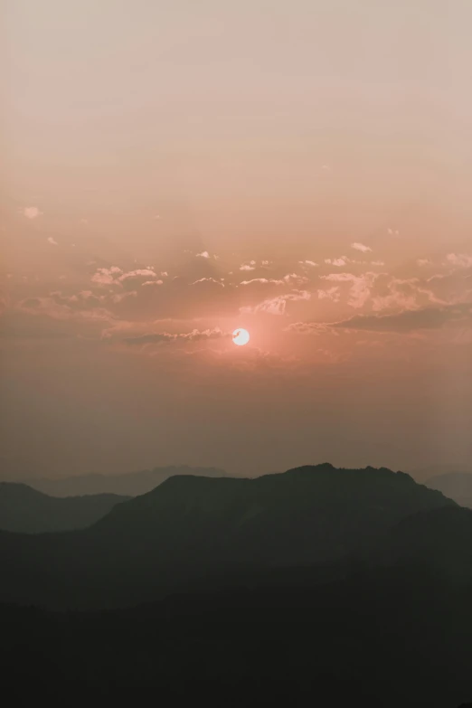 the sun setting over a mountain range with several silhouetted hills in the foreground