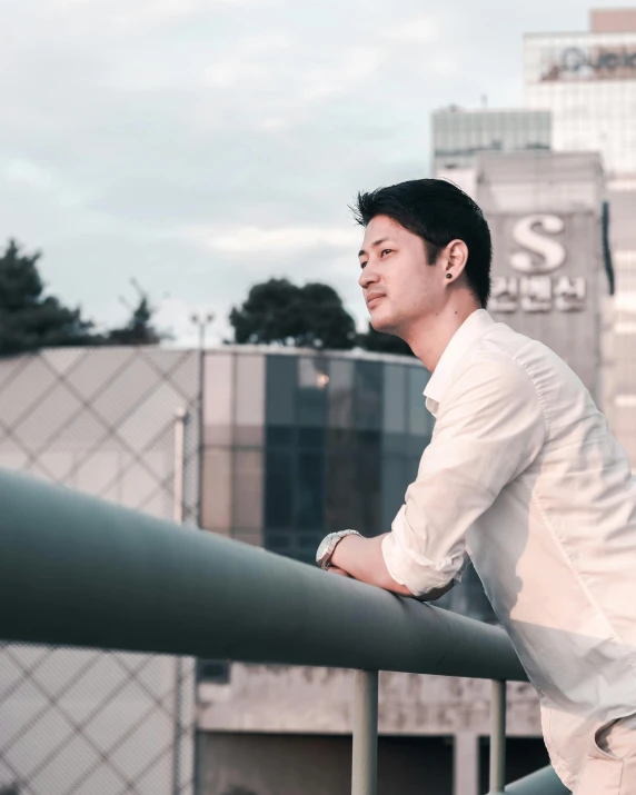 a young asian man leaning against the railing of an apartment building