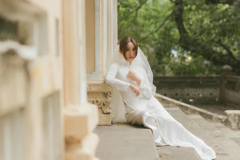 a woman wearing a white wedding gown sitting on the front porch of a house