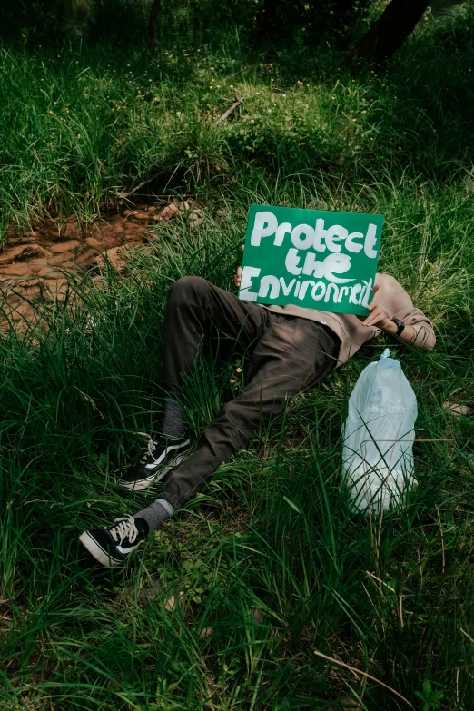 a man with a protest sign on his head lies in grass holding a water bottle