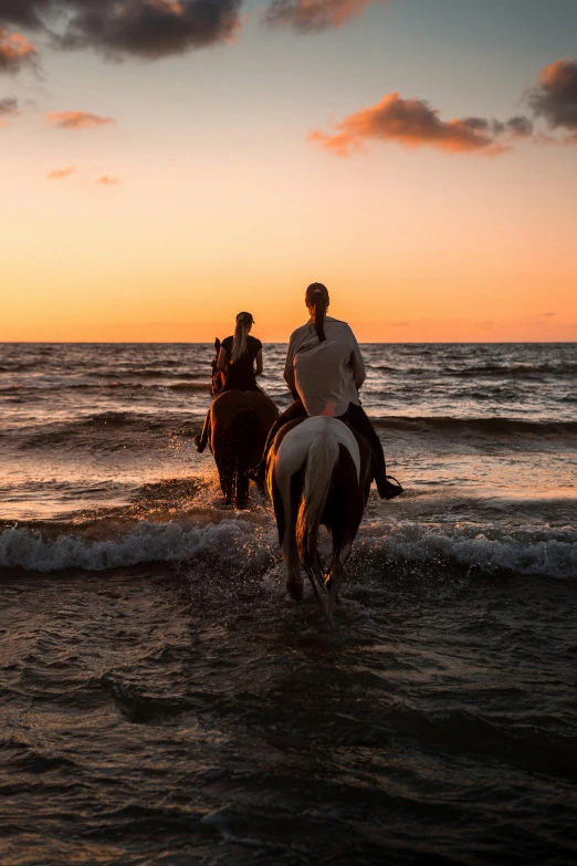 people riding horses into the ocean at sunset