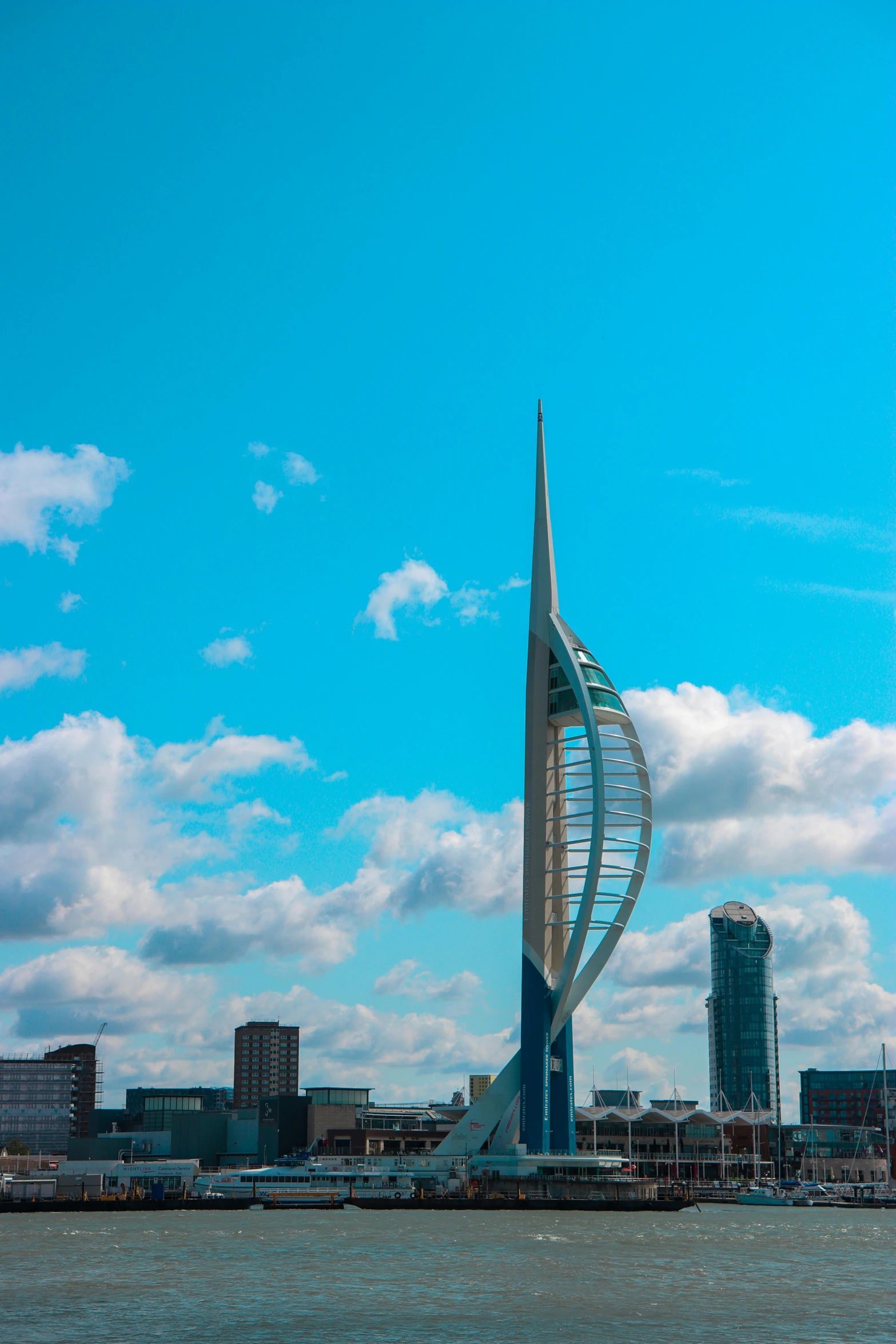 a tall building with a spiraly spire stands on a body of water