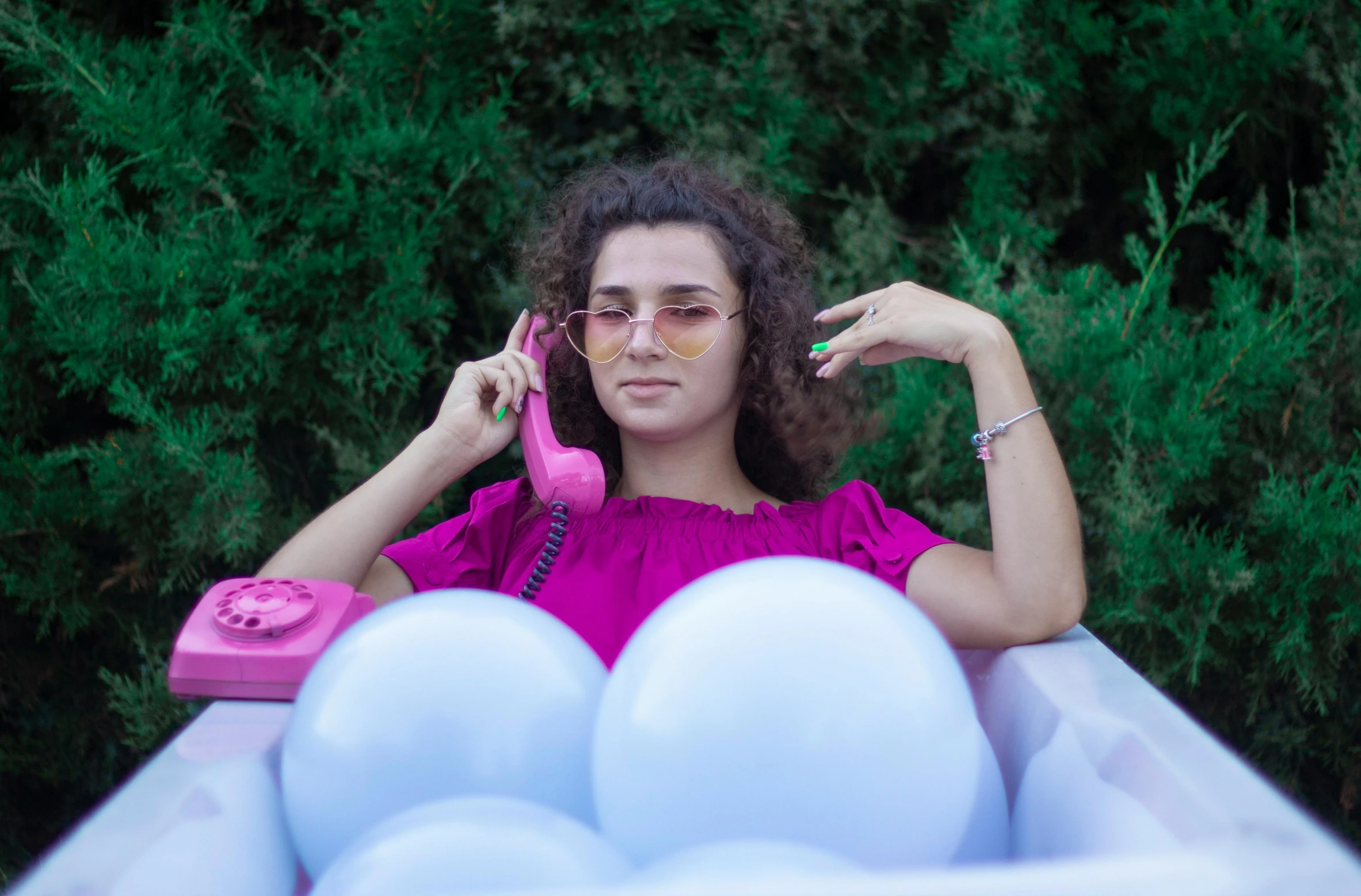 a woman in pink talking on the phone next to balloons