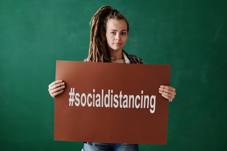 a woman in ripped jeans and striped shirt holding a sign with social distancing printed on it