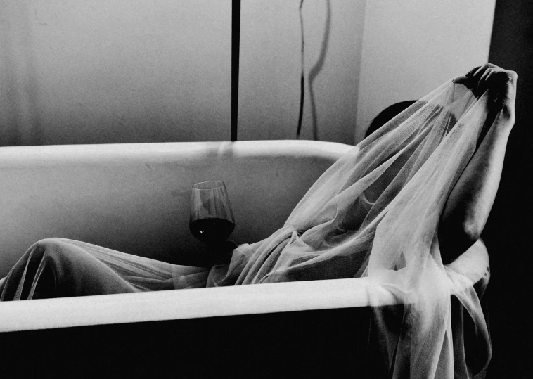 a person laying in a bath with their arm wrapped over a glass