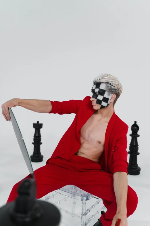 a man with a checkered mask is sitting on top of a giant chess set