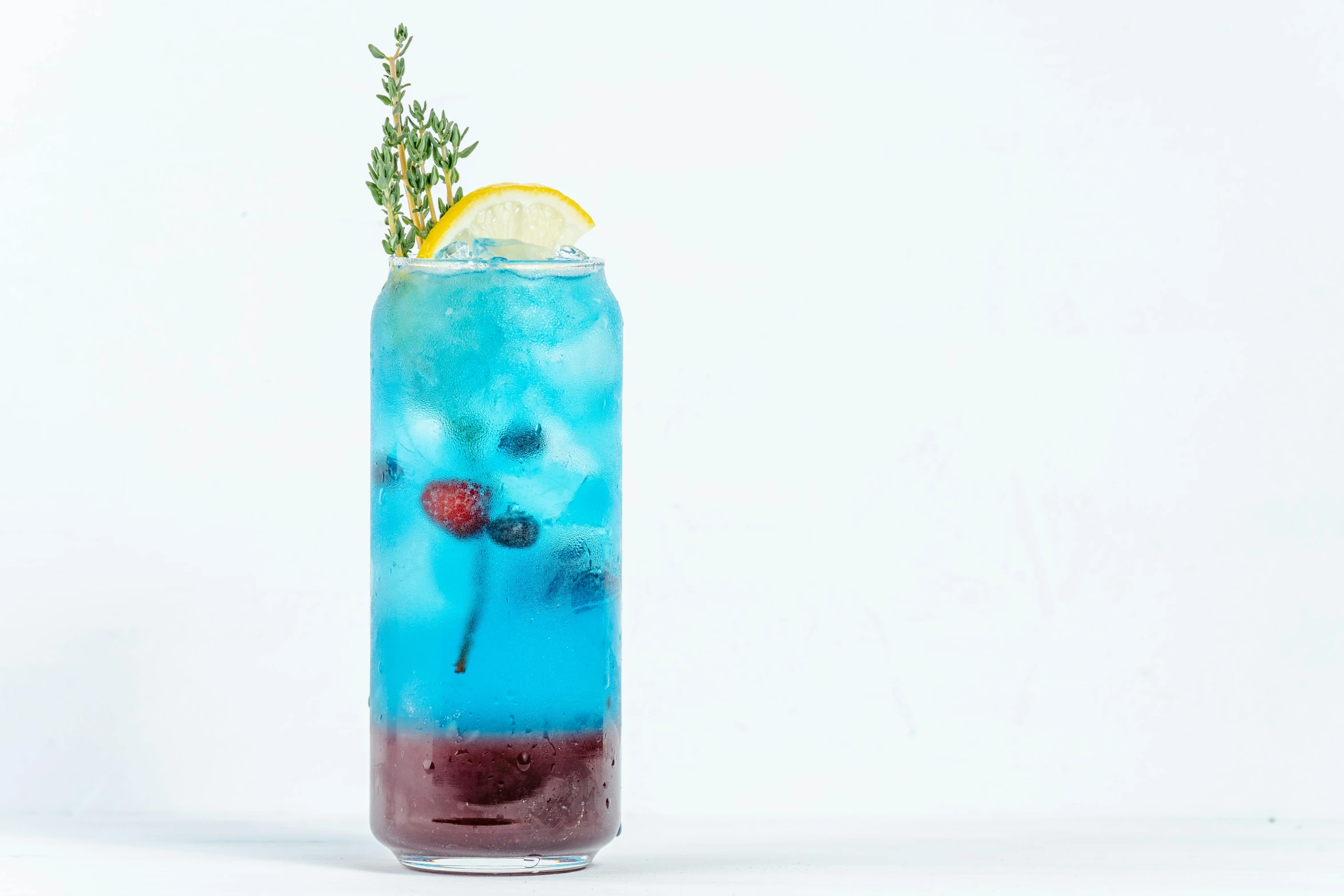 a blue drink with berries in it, garnished with a lemon slice