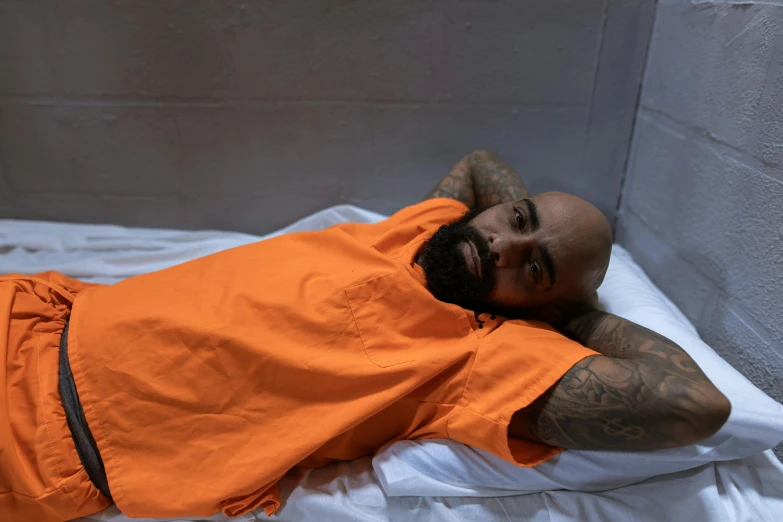 a young man wearing an orange shirt is sleeping on a white blanket