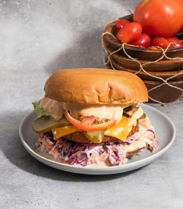 a white plate holding a large sandwich, a basket of tomatoes and other vegetables