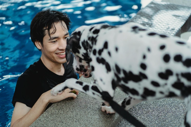 a smiling man holds his dog next to a pool