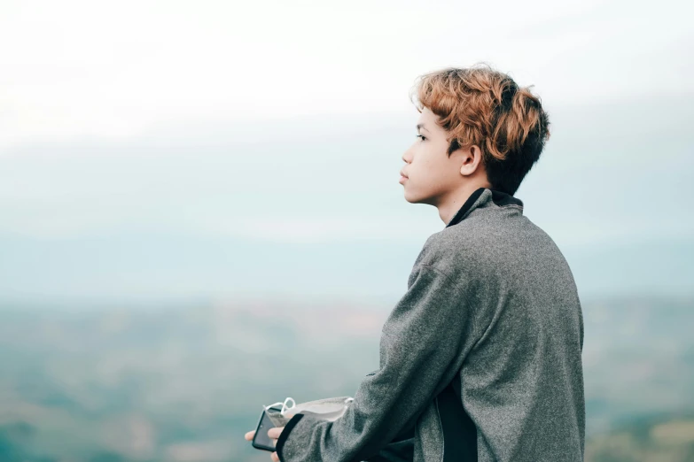 a boy with his hands in his pockets looking at the mountains