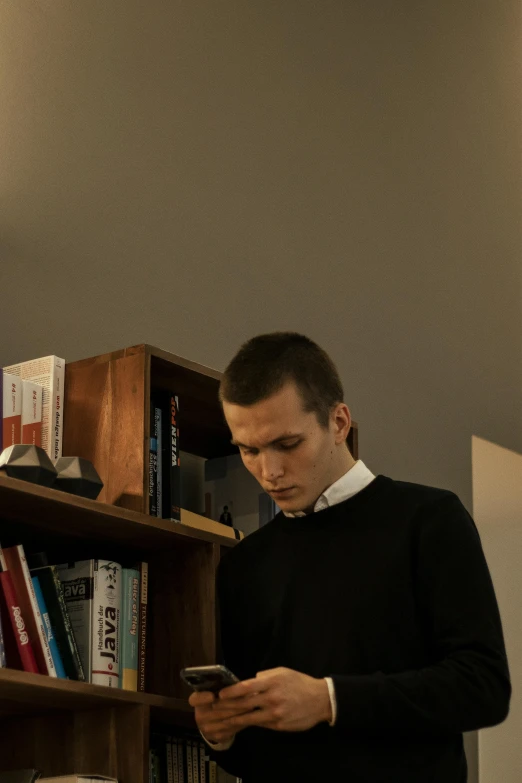 the man is checking his cell phone beside the bookshelf