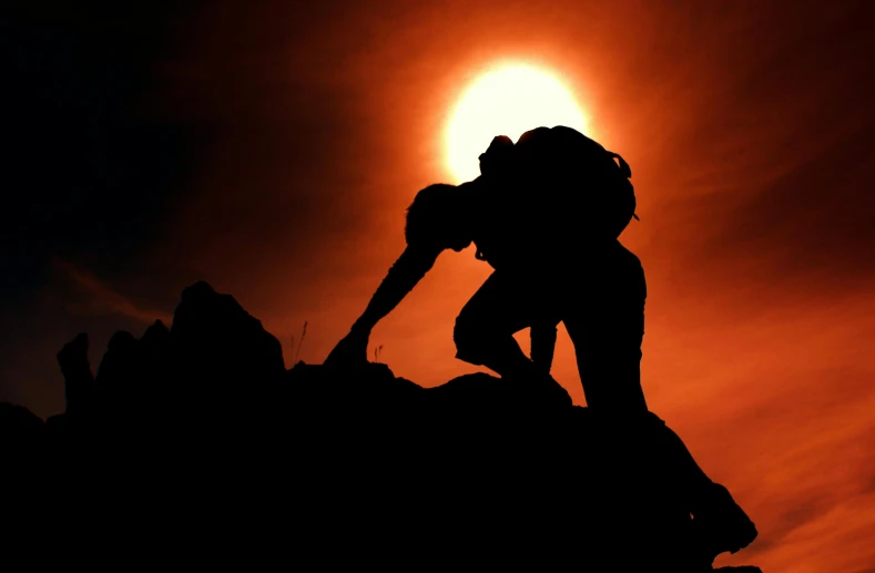 a silhouette of a person climbing up a hill at sunset