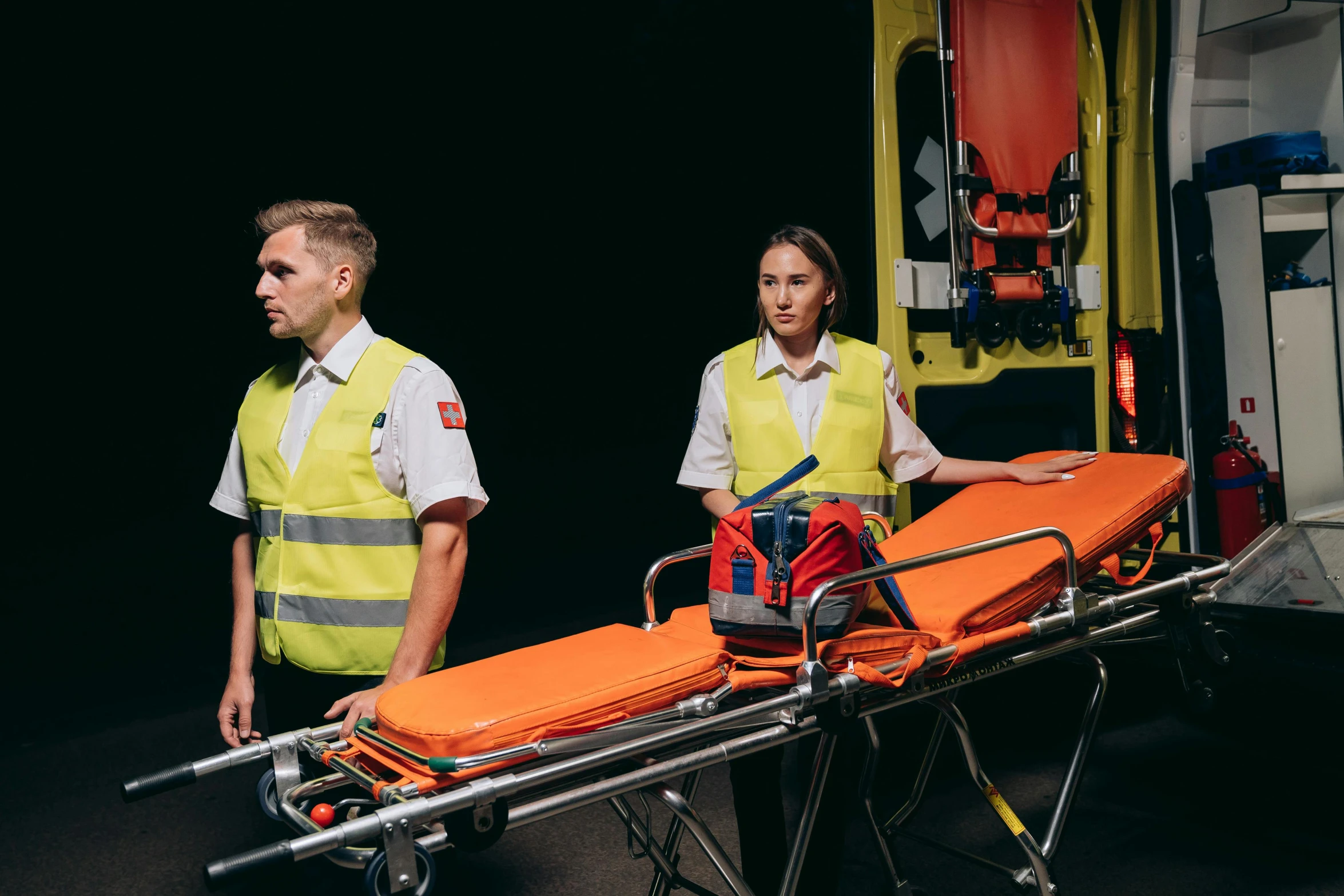 two medical personnel are loading an orange stretcher