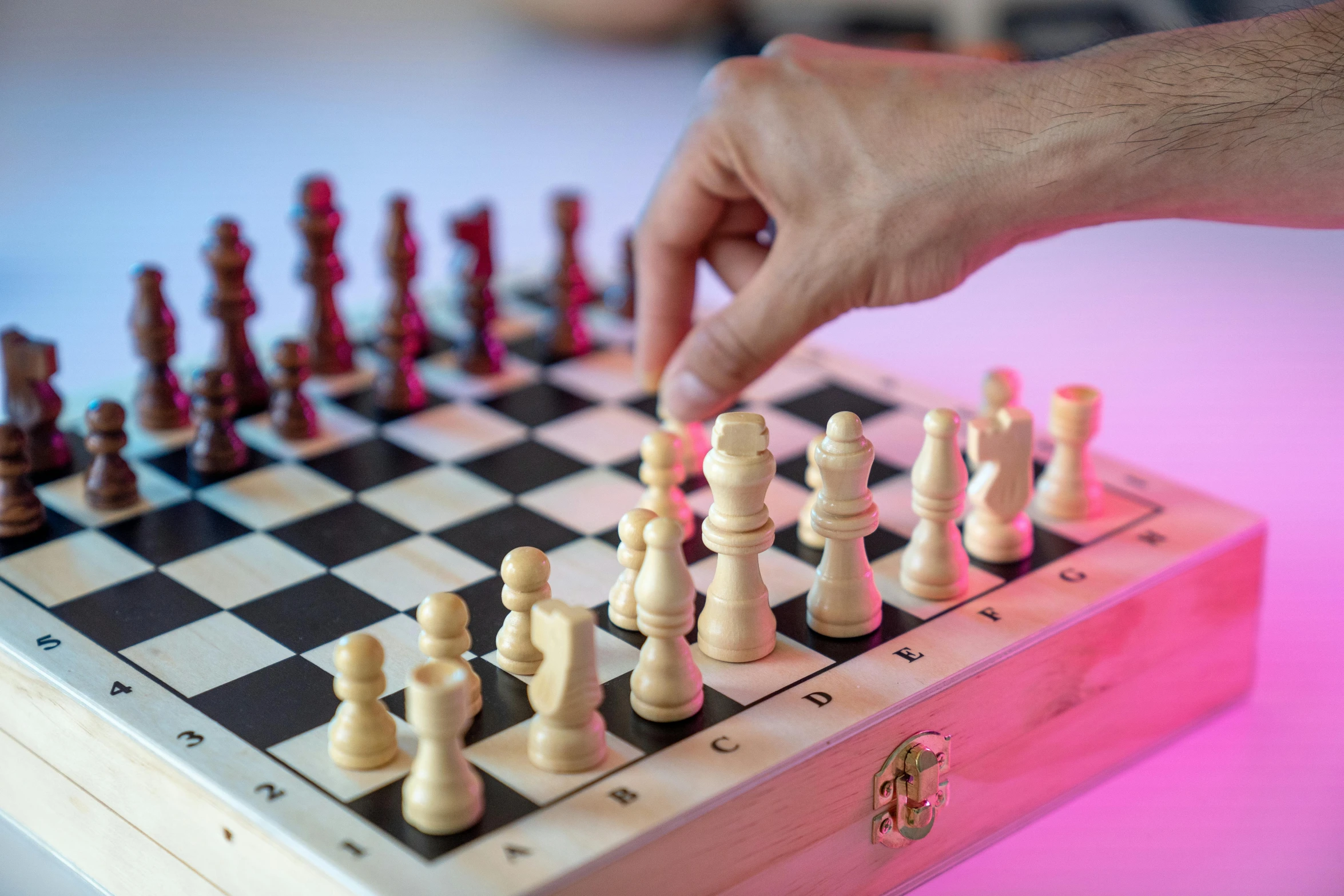 a wooden chess board with a hand reaching for it