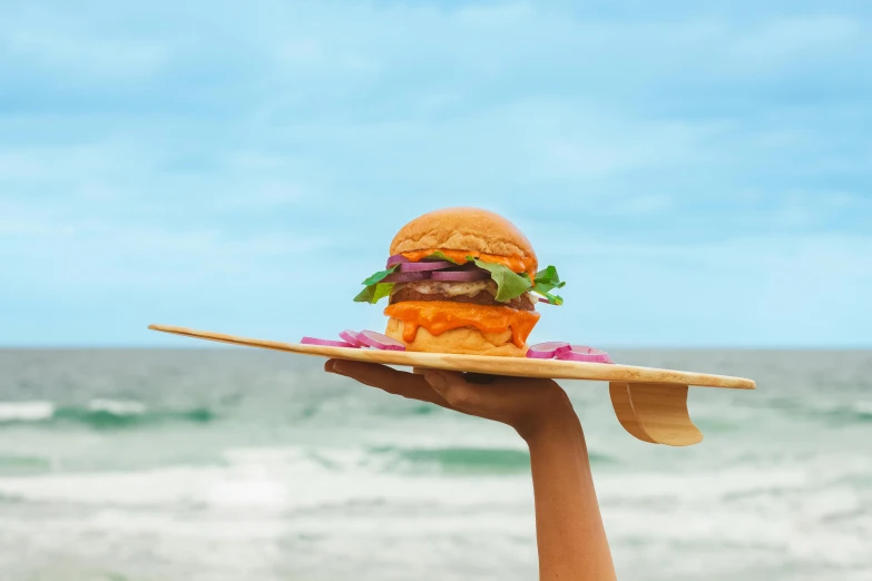 a hamburger is on a plate and there is a wooden board near the water