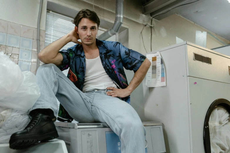 the man is sitting on top of the dryer and talking on a cell phone