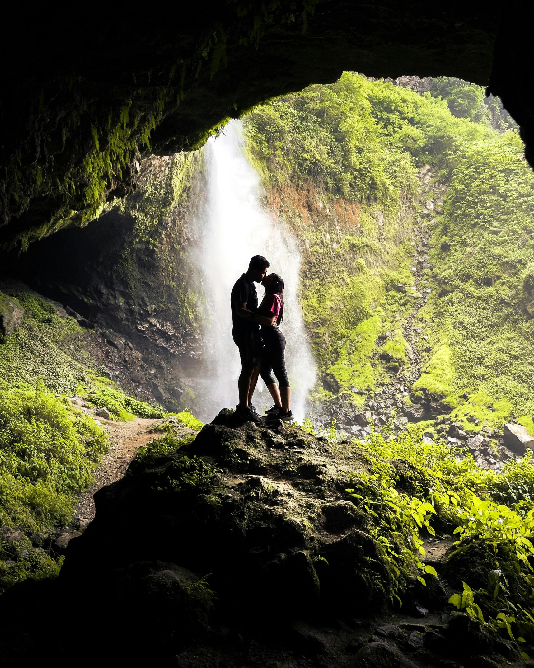 two people standing next to each other in front of a waterfall