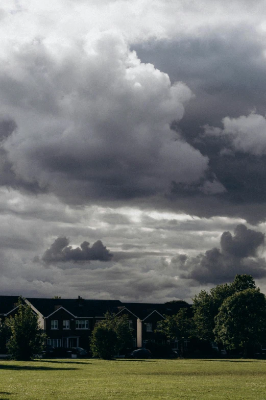 large clouds loom over a residential complex and grass