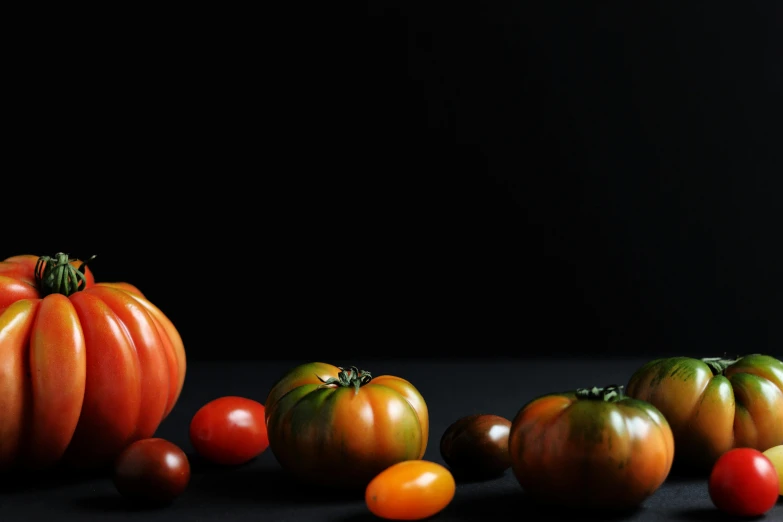 tomatoes, some oranges and one green one against black background