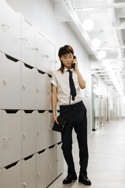 asian man leaning against a wall talking on a cellphone