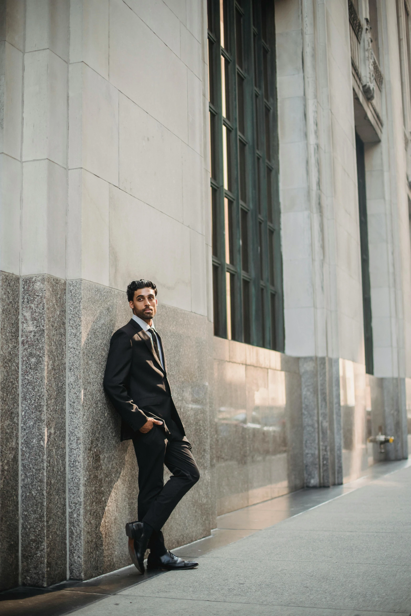 a man in a suit leans against a concrete wall