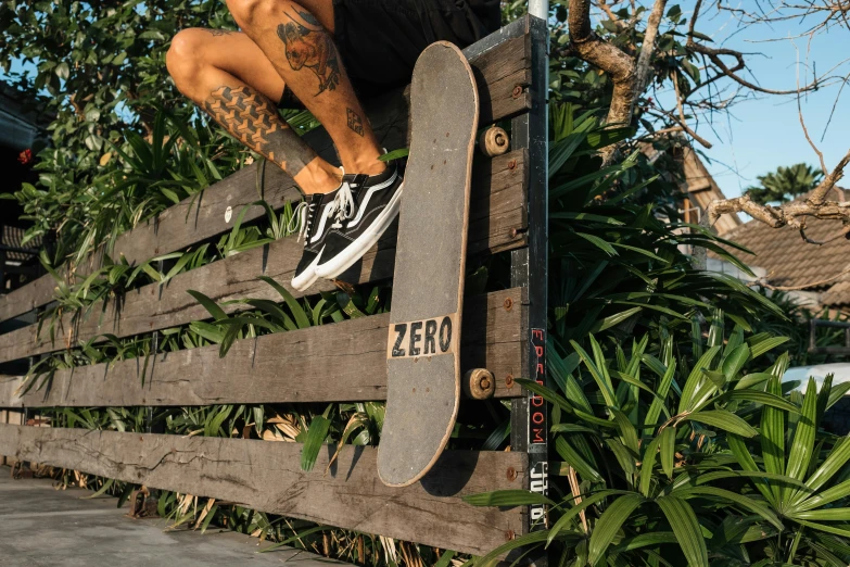 a man holding up his skateboard while sitting on a fence