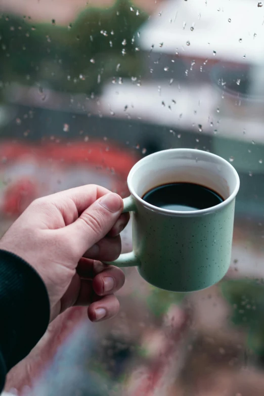 a man holding onto his cup by the window