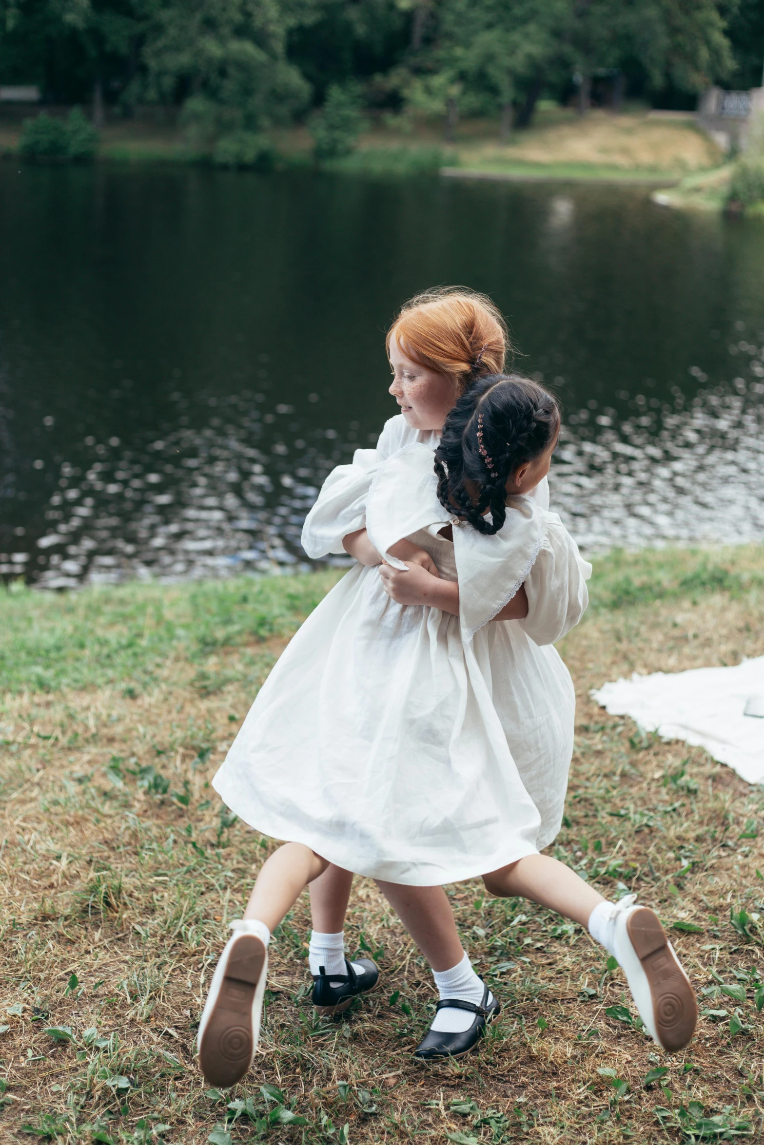 two little girls hugging each other in front of a lake