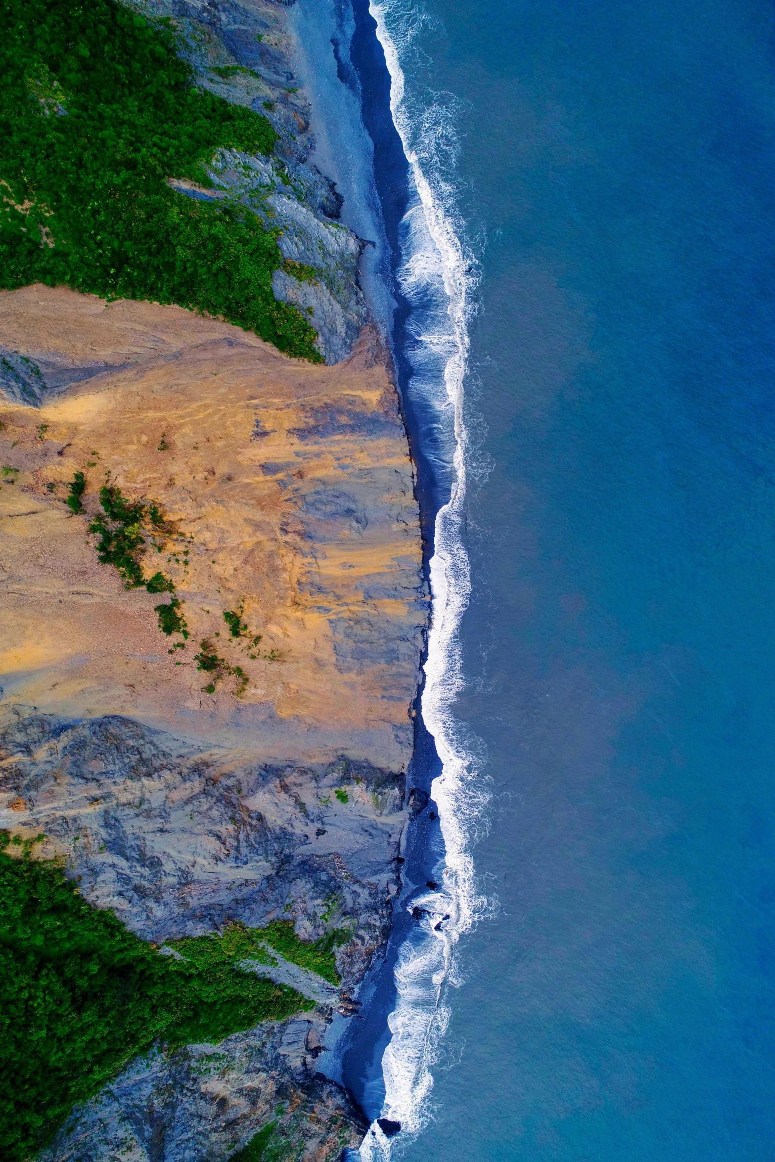 an aerial view of the beach and ocean, looking down on sand, rocks and plants