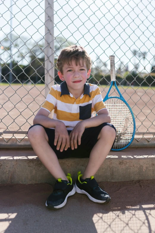 a  wearing black shorts is sitting against a fence with a tennis racket