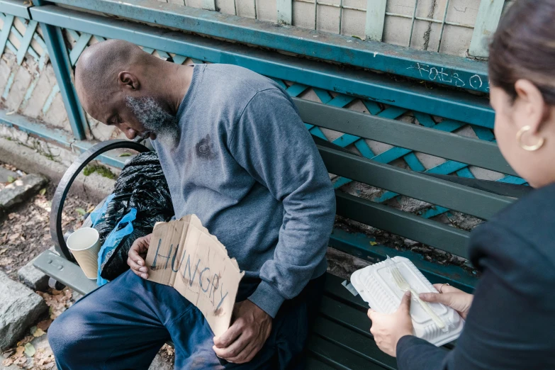 two people sitting on a bench with a man handing an empty box