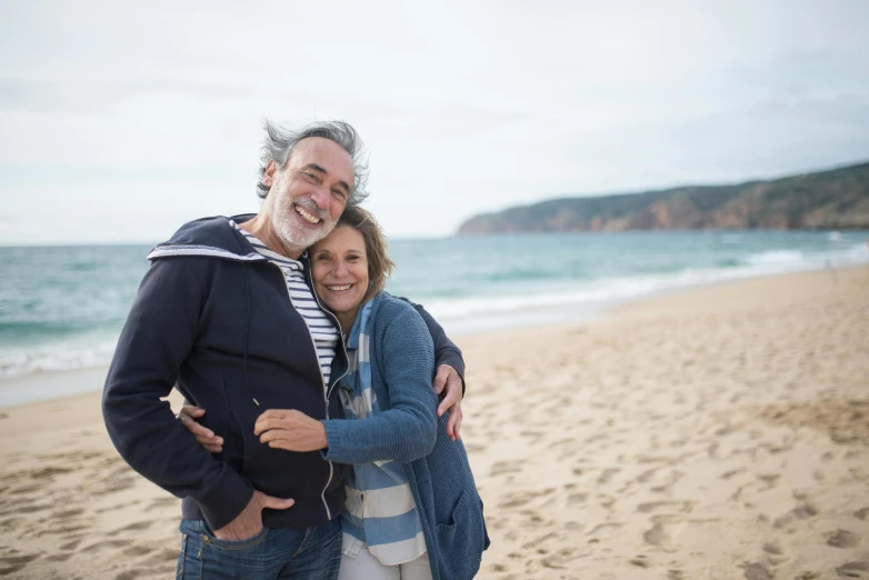 two people standing together on the beach next to the ocean