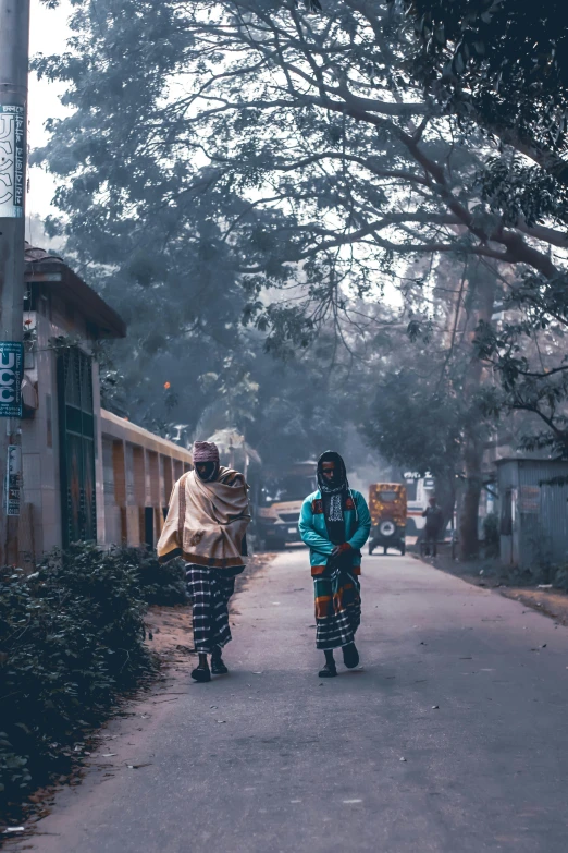 two people walking down a street near bushes and trees