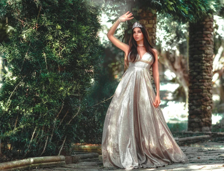 a model in a white and gold dress stands in a forest