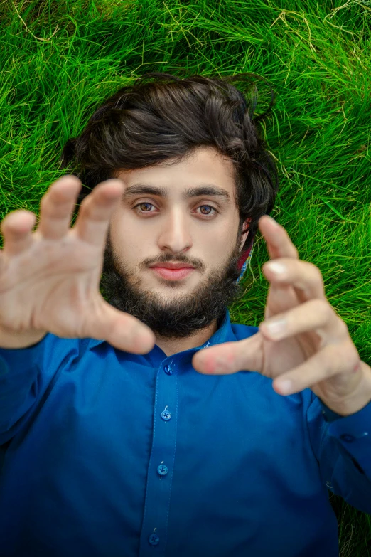 man in blue shirt laying on grass with hand extended