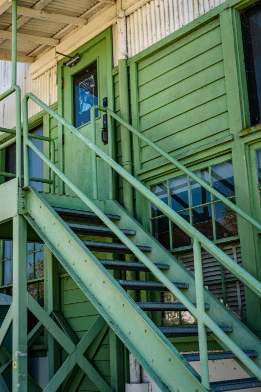 the green railing is set high to the wall and the green door is at the top of the building